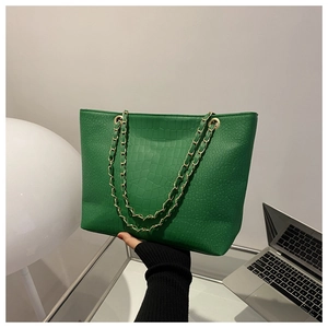 Detail view of the green crocodile pattern texture and gold chain strap on the tote bag