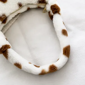Close-up of plush faux fur handbag with cow print pattern and premium gold zipper detail