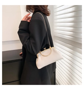 Detail der cremefarbenen Plissee-Clutch mit goldener Rundgriff und Kettenriemen am Modell