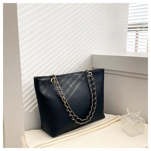 Detail of black tote bag featuring embossed snake texture and gold woven chain strap
