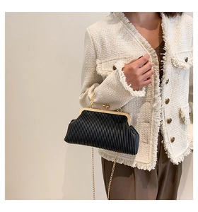 Detail einer schwarzen Plissee-Clutch mit goldenem Verschluss und feiner Kette