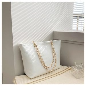 Detail of white snakeskin texture tote with gold chain strap in aesthetic natural light