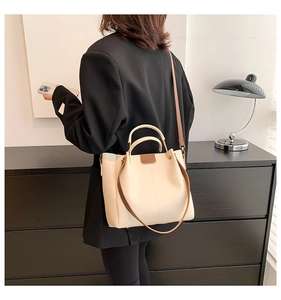 Side view of a cream tote bag with brown leather straps worn over a black blazer