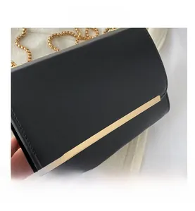 Détail de la texture en similicuir noir avec barre dorée et bandoulière chaîne