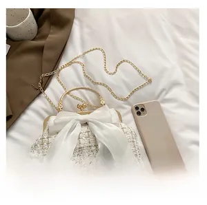 Close-up of white tweed handbag featuring a large chiffon bow and gold ring handle