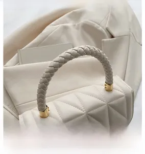 Detail of cream quilted handbag featuring woven handle and gold hardware on blazer