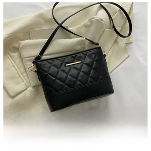 Detailed view of black quilted crossbody bag with gold zipper on beige blazer background