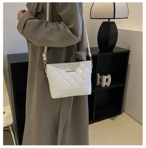 Detail of white quilted crossbody bag with gold hardware shown on person side view