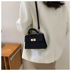 Detail of elegant black leather crossbody bag with gold twist lock on stylish woman