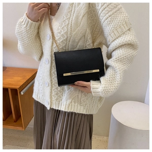 Detalle de bolso bandolera negro con cadena dorada y adorno metálico lucido por una modelo
