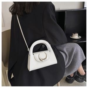 Chic white crossbody bag with silver crescent buckle on a marble table with dessert