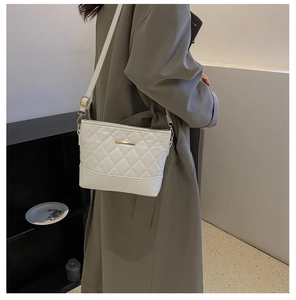 Close-up of white quilted crossbody bag with gold metal trim worn by model in minimalist setting