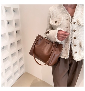 Detailed side view of brown tote bag featuring vertical stitching and golden metal handles