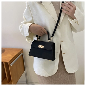 Detail of a chic black leather crossbody bag with gold lock buckle and top handle grip