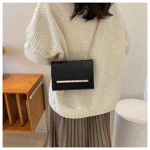 Detalle de bolso bandolera negro en piel sintética con elegante barra dorada y tira de cadena