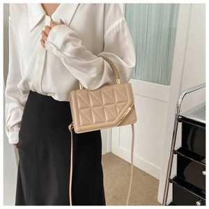 Close-up of beige quilted crossbody bag featuring gold hardware and a woven handle