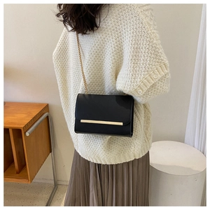 Detalle de bolso bandolera negro con adorno metálico dorado y cadena llevado por modelo