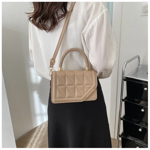 Close-up of a beige quilted crossbody bag with a woven handle and gold hardware on model