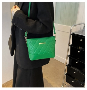 Close-up of vibrant green quilted hobo bag featuring gold metal bar and adjustable strap