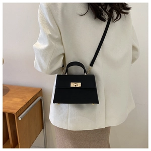 Dettaglio di una borsa a trapezio in pelle nera opaca con chiusura girevole dorata e tracolla