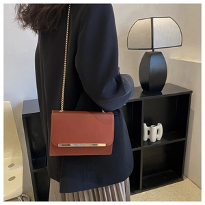 Bolso bandolera rojo ladrillo con cadena dorada usado por una modelo en una habitación
