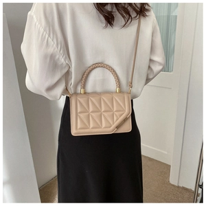 Detail view of beige quilted handbag featuring woven handle and metal trim on model