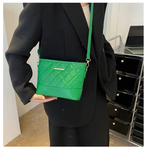 Detail of green quilted crossbody bag with gold hardware on black wool coat