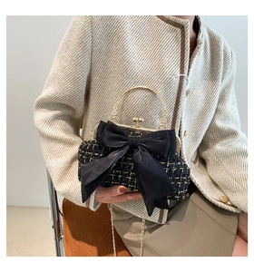 Detail of tweed crossbody bag with a large black satin bow and gold chain on model