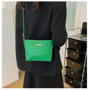 Detail view of vibrant green quilted crossbody bag with gold metal clasp on black coat