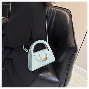 Detail of mint green leather handbag with crescent metal buckle on a black leather couch