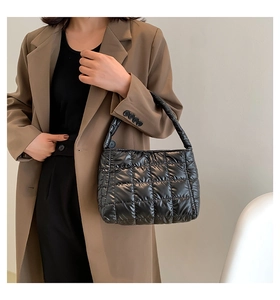 Detail of a black quilted puffer tote bag with glossy finish and square stitch patterns