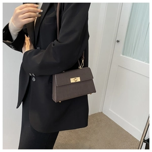 Detail of dark brown crocodile embossed leather handbag with golden twist lock closure