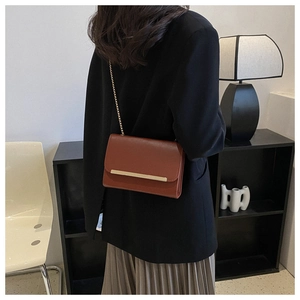 Detalle de bolso bandolera de cuero PU marrón con cadena dorada lucido por una modelo