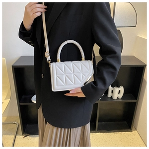 Detail of white quilted crossbody bag with woven handle and gold-tone hardware accents