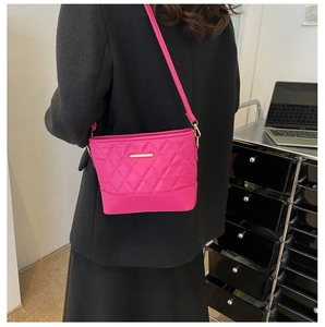 Detail shot of a hot pink quilted crossbody bag with a gold metal bar and thin shoulder strap