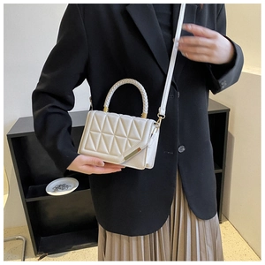 Detail of white quilted handbag with woven handle and gold hardware on model in suit