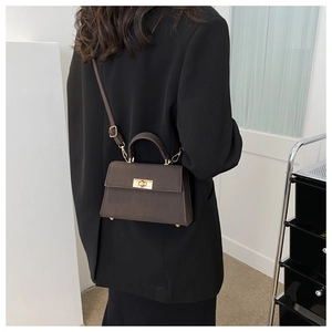 Dettaglio borsa a tracolla in pelle marrone scuro con chiusura dorata su blazer nero