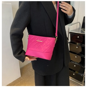 Detail of rose red quilted crossbody bag with gold metal hardware and adjustable strap
