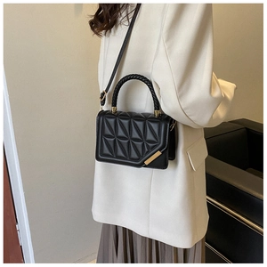 Detail of black quilted crossbody bag with braided handle and gold metal trim