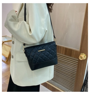 Close-up of black quilted hobo bag with gold chain strap on white blazer outfit
