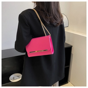 Bolso magenta con cadena dorada llevado sobre una chaqueta negra vista de detalle