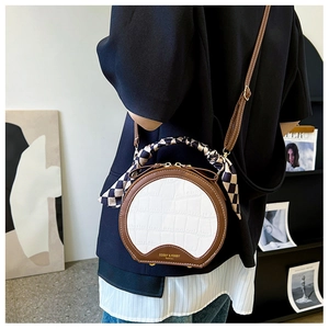 Detail of round handbag featuring crocodile pattern, scarf-wrapped handle and brand logo