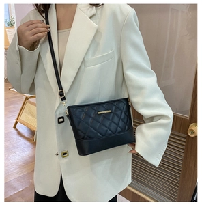 Detail of vintage quilted crossbody bag with gold hardware on white blazer model