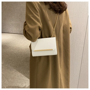Detalle de bolso blanco rectangular con solapa y cadena dorada mostrado sobre modelo