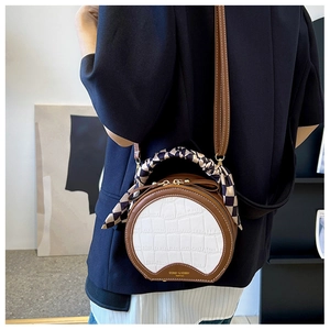 Detail of round crossbody bag with crocodile texture and decorative silk scarf on the strap