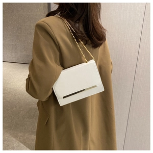 Detalle de bolso de hombro blanco minimalista con cadena dorada y acabado metálico
