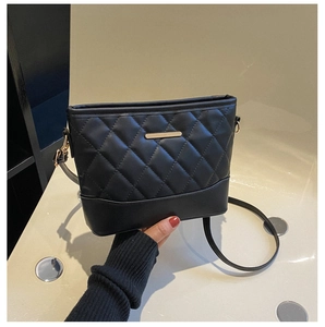 Detail view of black quilted faux leather crossbody bag with minimalist gold metal bar logo