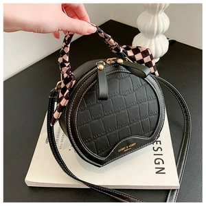 Close-up of black crocodile-embossed round bag featuring decorative silk scarf handle