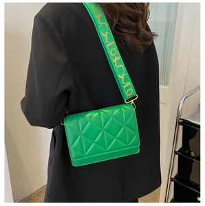 Detail of green quilted crossbody bag with a wide patterned strap on black blazer