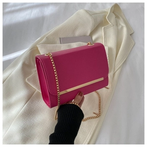 Detalle de bolso bandolera rosa fucsia con cadena dorada sobre blazer blanco